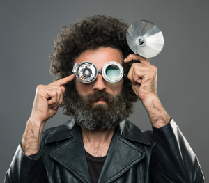 A man wearing a unique pair of mechanical glasses with a satellite dish attached. The device looks like a prototype of the man's invention.
