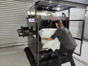 Photo of a Modix BIG-Meter 3D printer. It's much larger than a home printer. The printer is taller than the man who is pulling a 3D printed object from it.